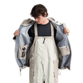 Open beige Analog Hardpack 3L Snowboard Jacket showing grey interior lining and internal pockets over matching bibs.
