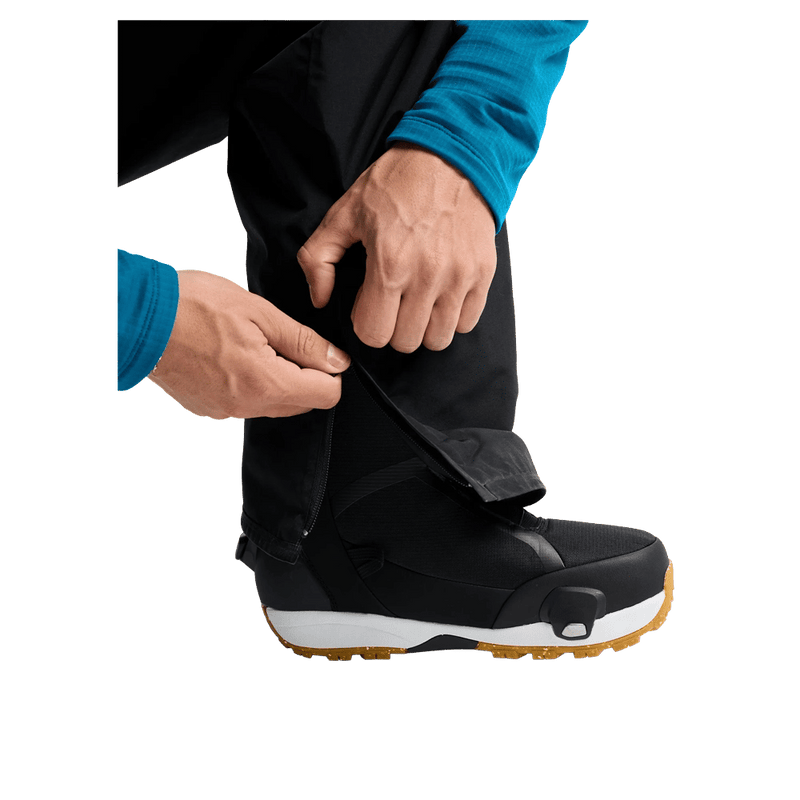 Black Burton AK Cyclic Gore-Tex snowboard pants cuff being pulled over a black and white snowboard boot.