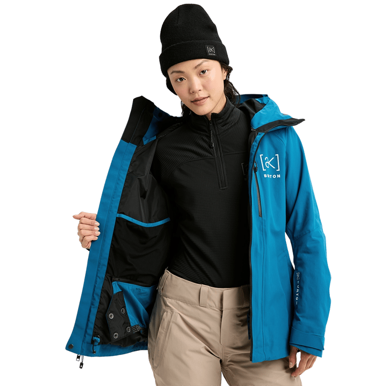 Woman wearing a blue Burton AK Upshift Gore-Tex 2L Snowboard Jacket unzipped to show the interior lining and mesh pocket.
