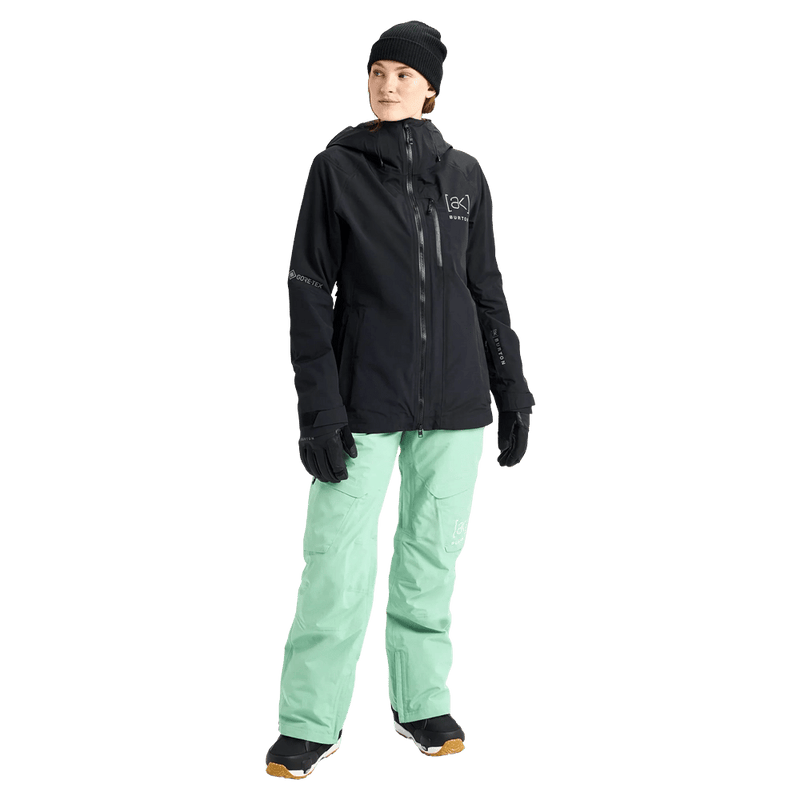 Black Burton AK Upshift Gore-Tex 2L women's snowboard jacket with hood and chest pocket, paired with mint green pants.