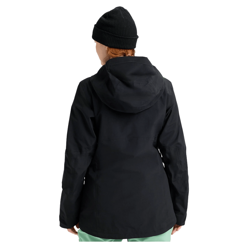 Rear view of a black Burton AK Upshift Gore-Tex 2L Women's Snowboard Jacket with a hood and black beanie.