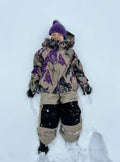Child wearing tan Burton Maven Bib Snowboard Pants with black knee patches lying in the snow.