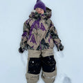 Child wearing tan Burton Maven Bib Snowboard Pants with black knee patches lying in the snow.