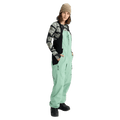Women's mint green Burton Reserve Bib snowboard pants with black side panels and zippered pockets on a model.