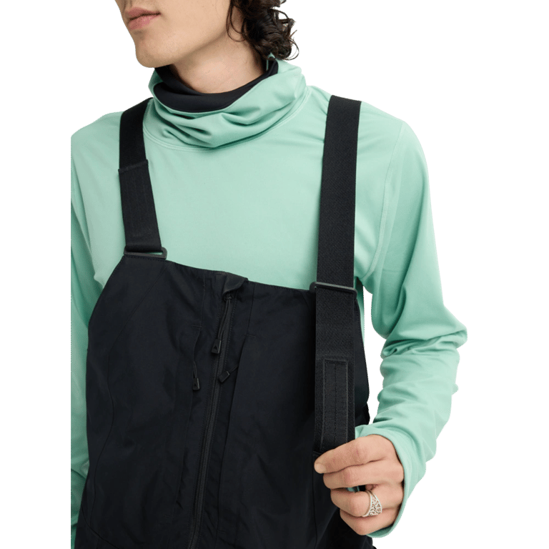 Black Burton Reserve bib snowboard pants with adjustable straps and front zipper over a mint green long-sleeve top.