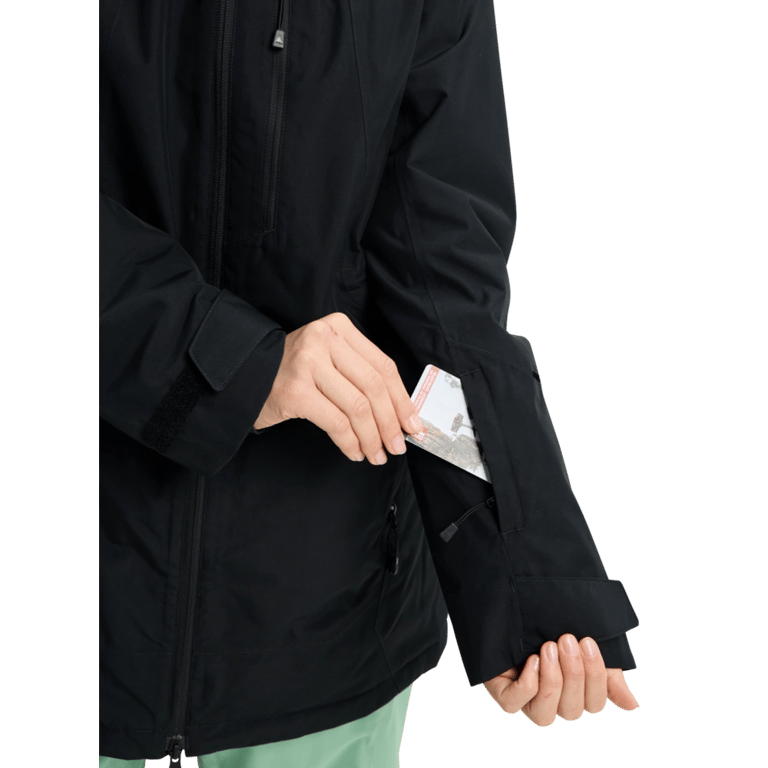 Black Burton Reserve Insulated Snowboard Jacket for women showing a lift pass being placed in a zippered sleeve pocket.