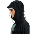 Profile of a woman in a black and green Burton Reserve Insulated Snowboard Jacket with hood up over a white beanie.