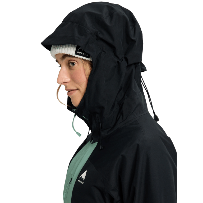 Profile of a woman in a black and green Burton Reserve Insulated Snowboard Jacket with hood up over a white beanie.