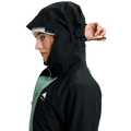 Woman wearing a black and sage green Burton Reserve Insulated Snowboard Jacket with the hood up and a white beanie.