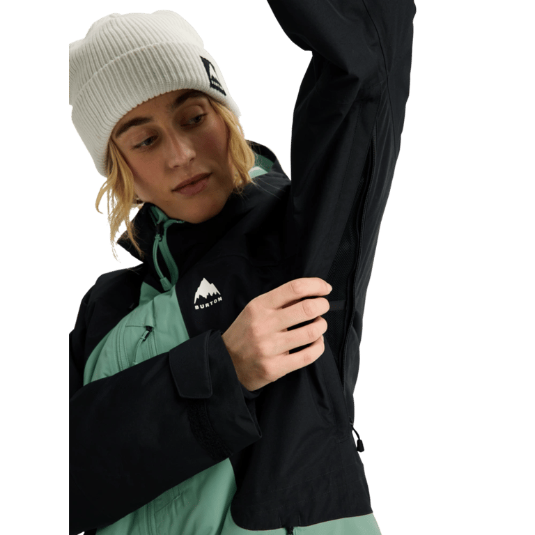 Woman wearing a black and mint green Burton Reserve snowboard jacket showing the underarm ventilation zipper.