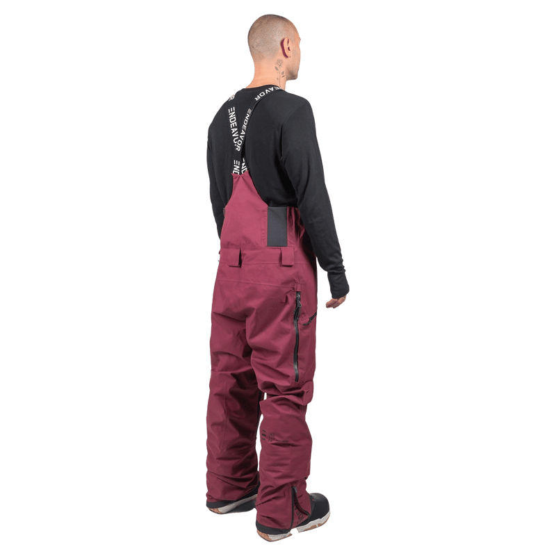 Rear view of maroon Endeavor 3L Shelter Bib Snowboard Pants with branded suspenders and side zippers.
