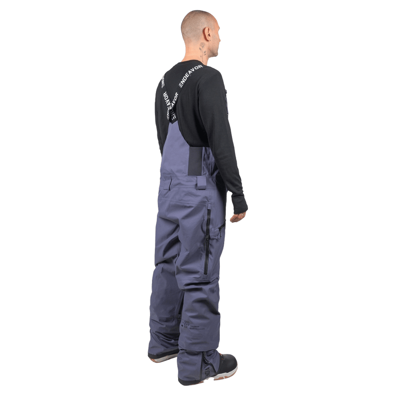 Rear view of slate blue Endeavor 3L Shelter Bib Snowboard Pants on a model with branded suspenders and side leg zipper.