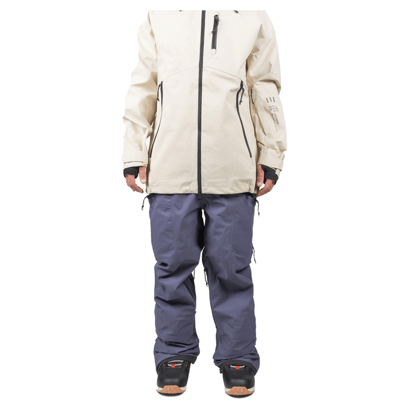Slate blue Endeavor 3L Shelter Bib Snowboard Pants worn with a cream jacket and black boots, front view.