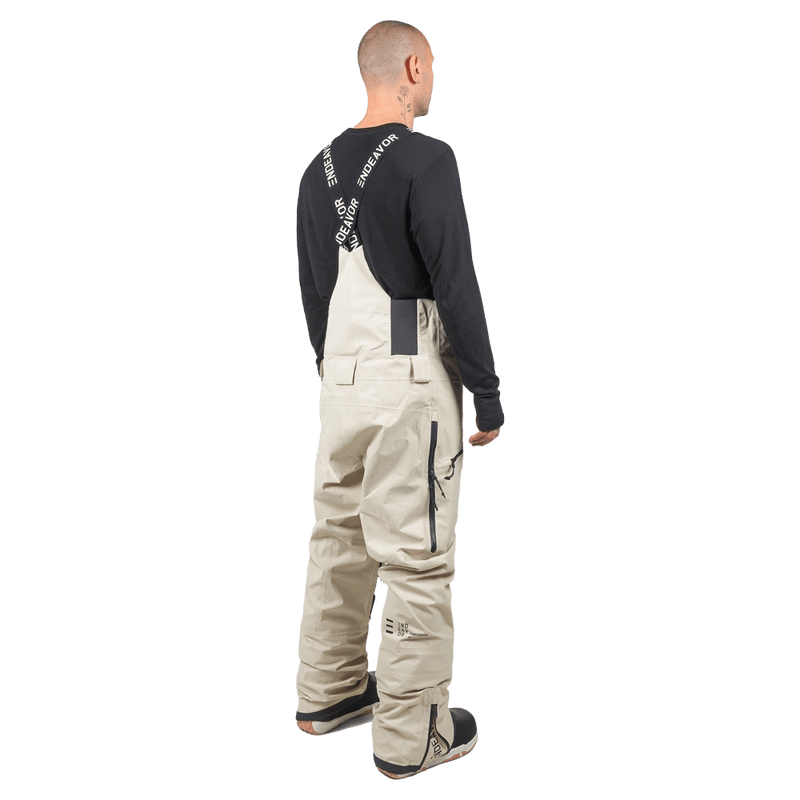 Rear view of beige Endeavor 3L Shelter Bib Snowboard Pants with black branded suspenders and side zippers.