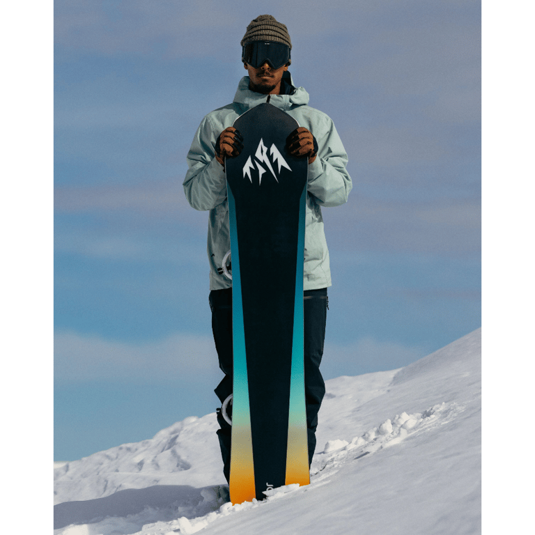 front view of Man standing on snow slope holding Jones 2027 Stratos Snowboard