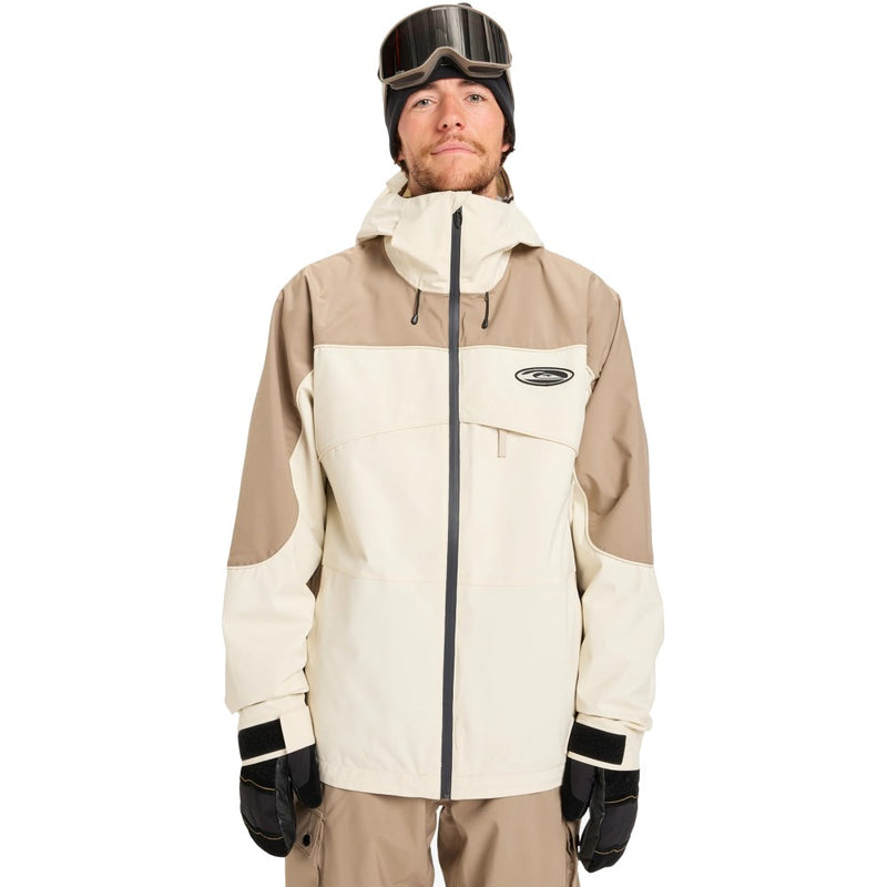 Man wearing a cream and tan Quiksilver Radicalo Snowboard Jacket with a hood, chest logo, and black center zipper.