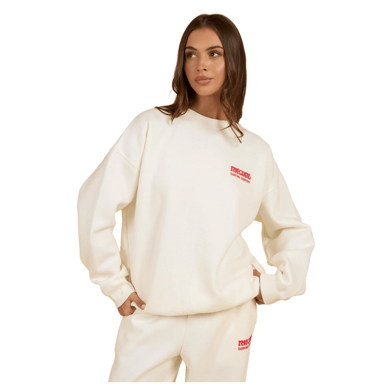 Woman wearing a cream Rip Curl Surf Puff Inspired Crew sweatshirt with a small red chest logo and matching track pants.