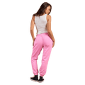 Woman from behind wearing bright pink Rip Curl trackpants with cuffed ankles, white tank top, and black sneakers.