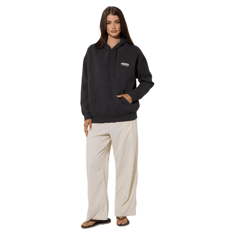 Woman wearing a charcoal Rip Curl Surf Revival Heritage Hoodie with a chest logo and cream wide-leg pants.