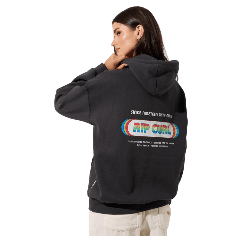 Back view of a woman wearing a charcoal grey Rip Curl Surf Revival Heritage Hoodie with a rainbow logo and retro graphics.