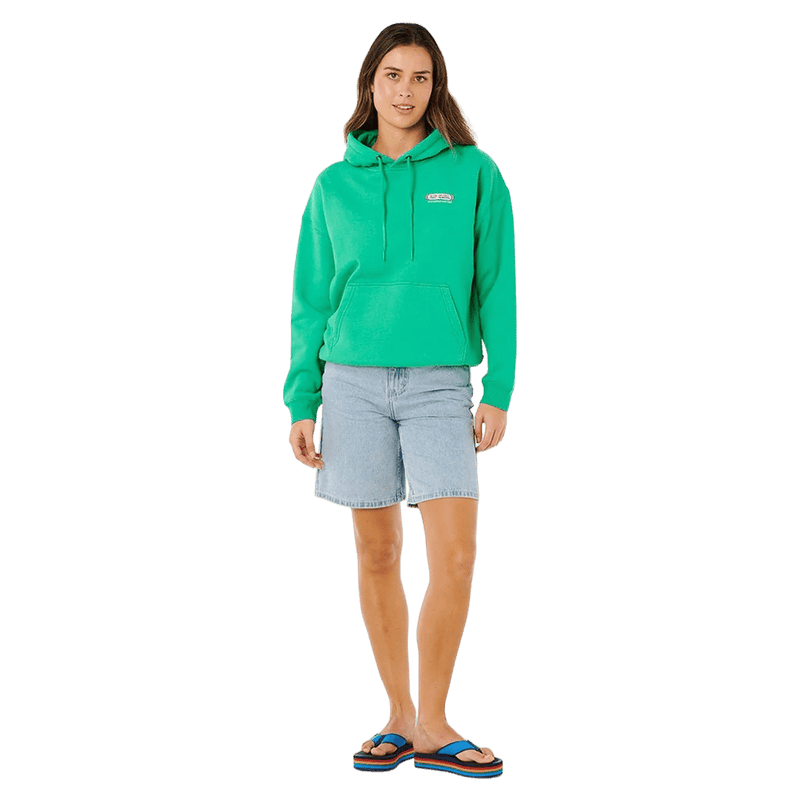 Woman wearing a bright green Rip Curl Surf Revival Heritage Hoodie with a front pocket and light blue denim shorts.