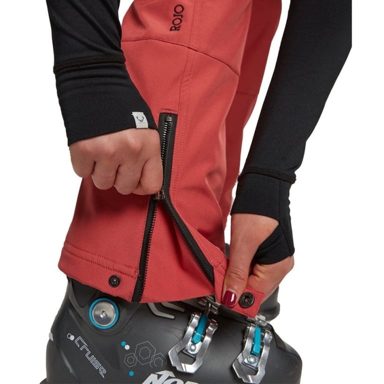 Close-up of red Rojo women's softshell ski pants showing the zippered ankle gusset over a ski boot.